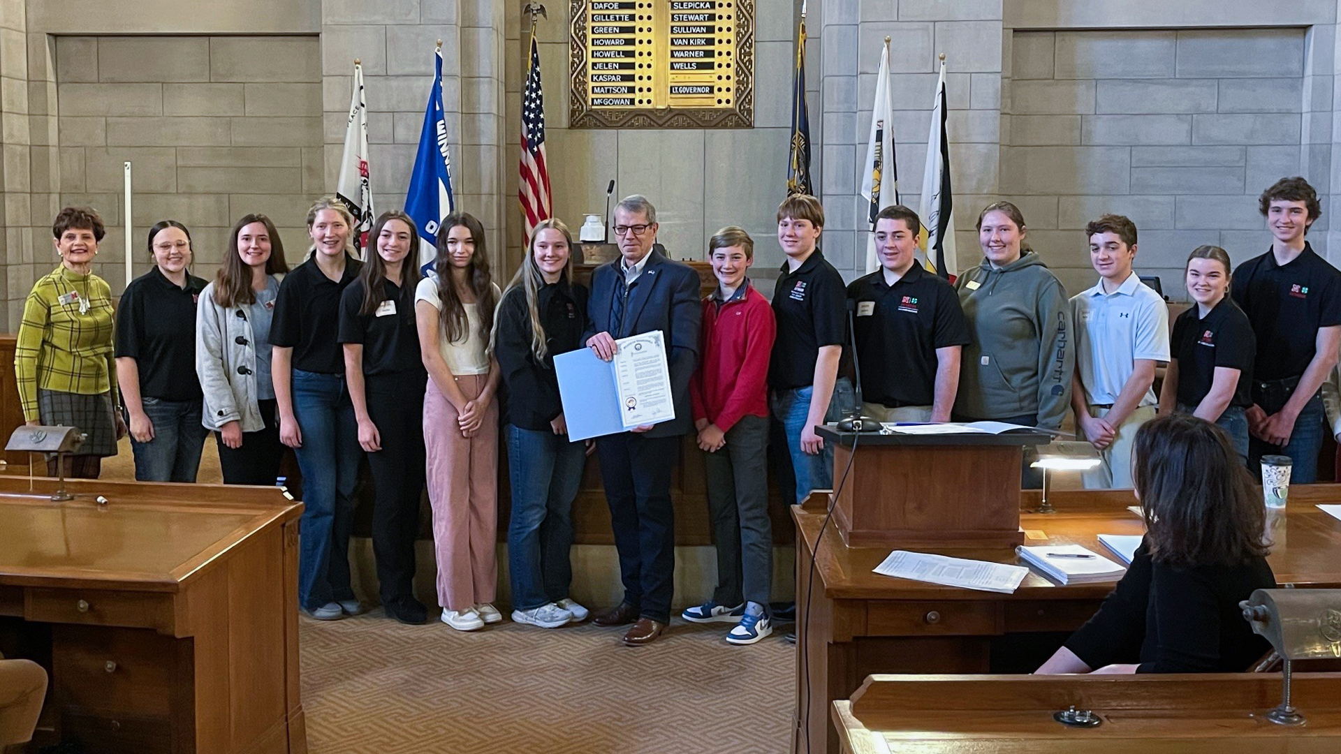 Gov. Jim Pillen holds a proclamation designating February as Nebraska 4-H Month, flanked by Kathleen Lodl (far left) and 13 youth ambassadors from Cass, Douglas, Sarpy and Washington counties at the Nebraska State Capitol.