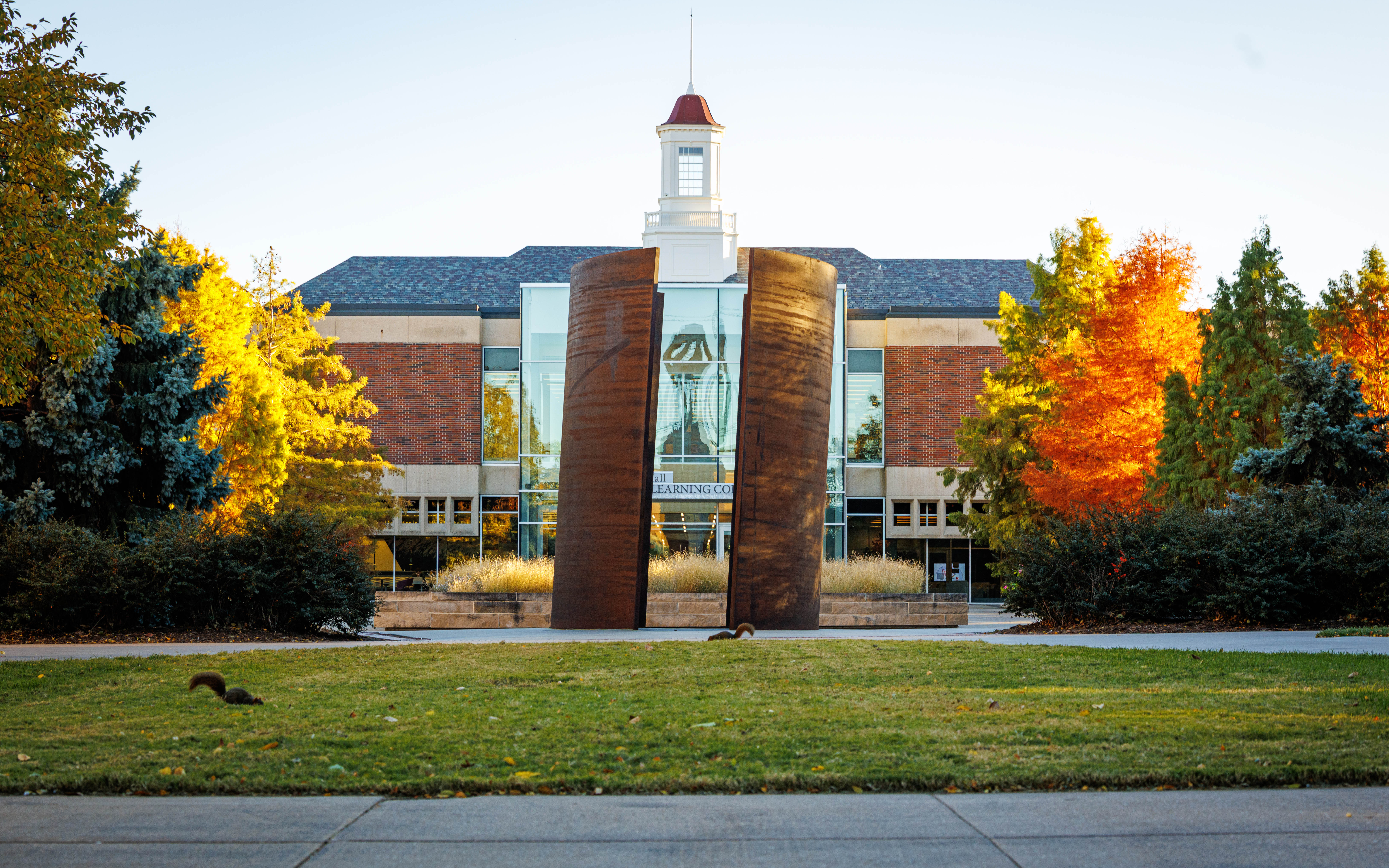 The "Greenpoint" sculpture is seen north of the Love Library cupola on a fall afternoon, as two squirrels scurry about in the grass.