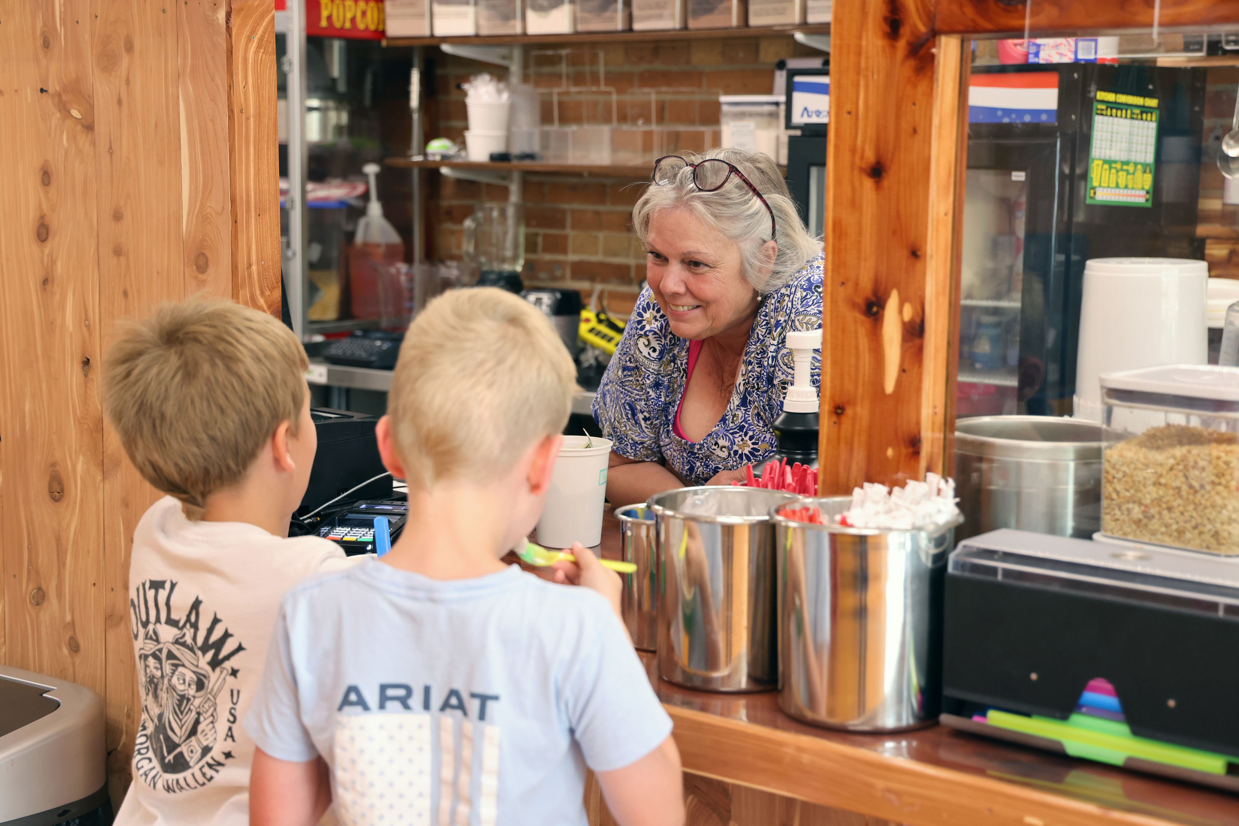 Two young boys buy ice cream from an older woman in a store.