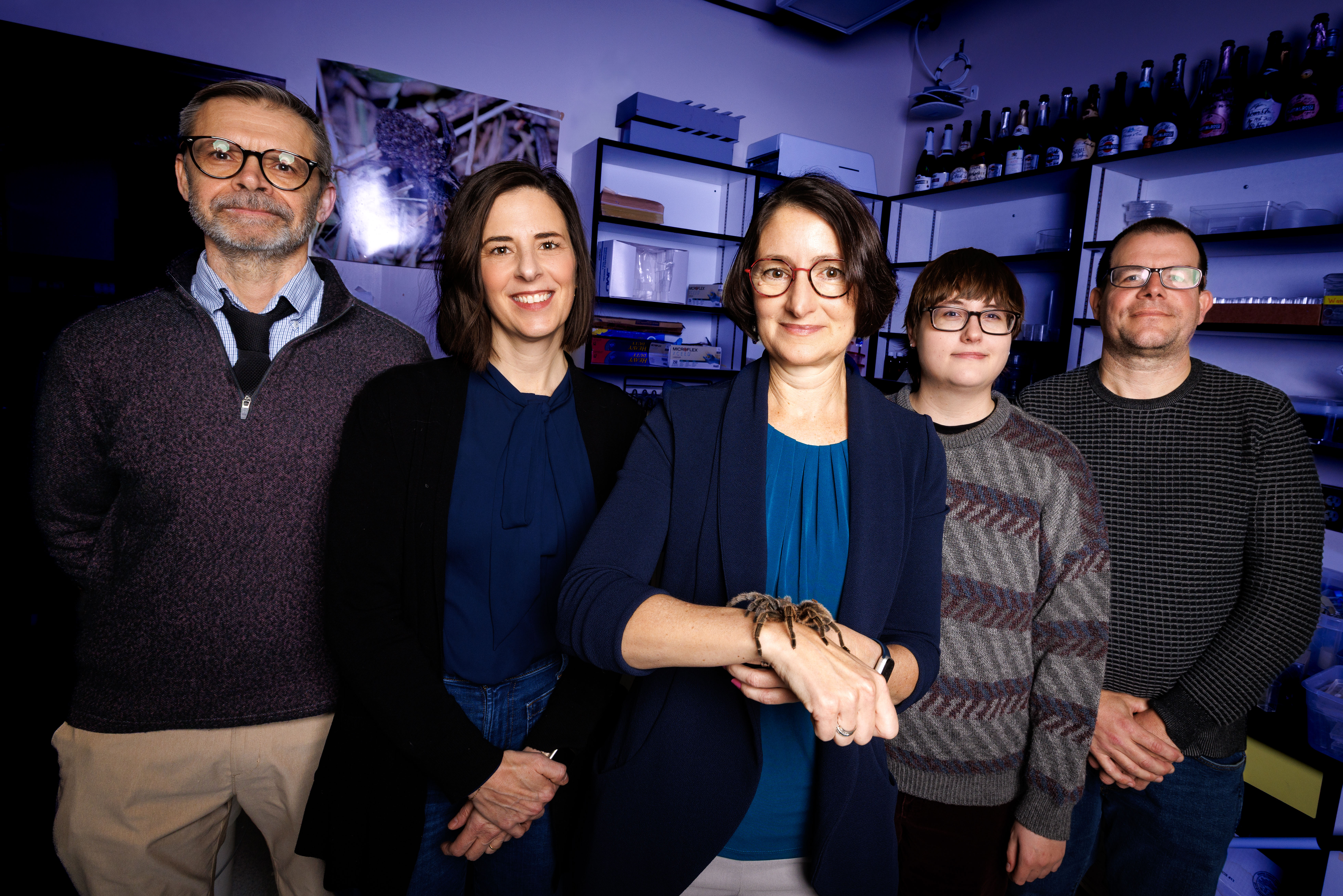 Husker researchers pose in a blue-lit lab. From left are: Kevin Smith, Leland J. and Dorothy H. Olson Professor of political science; Heather Akin, associate professor of agricultural leadership, education and communication; Eileen Hebets, George Holmes Professor of biological sciences; Emma Brase, graduate student in psychology; and Mike Dodd, professor of psychology. Hebets has a tarantula on her right wrist.