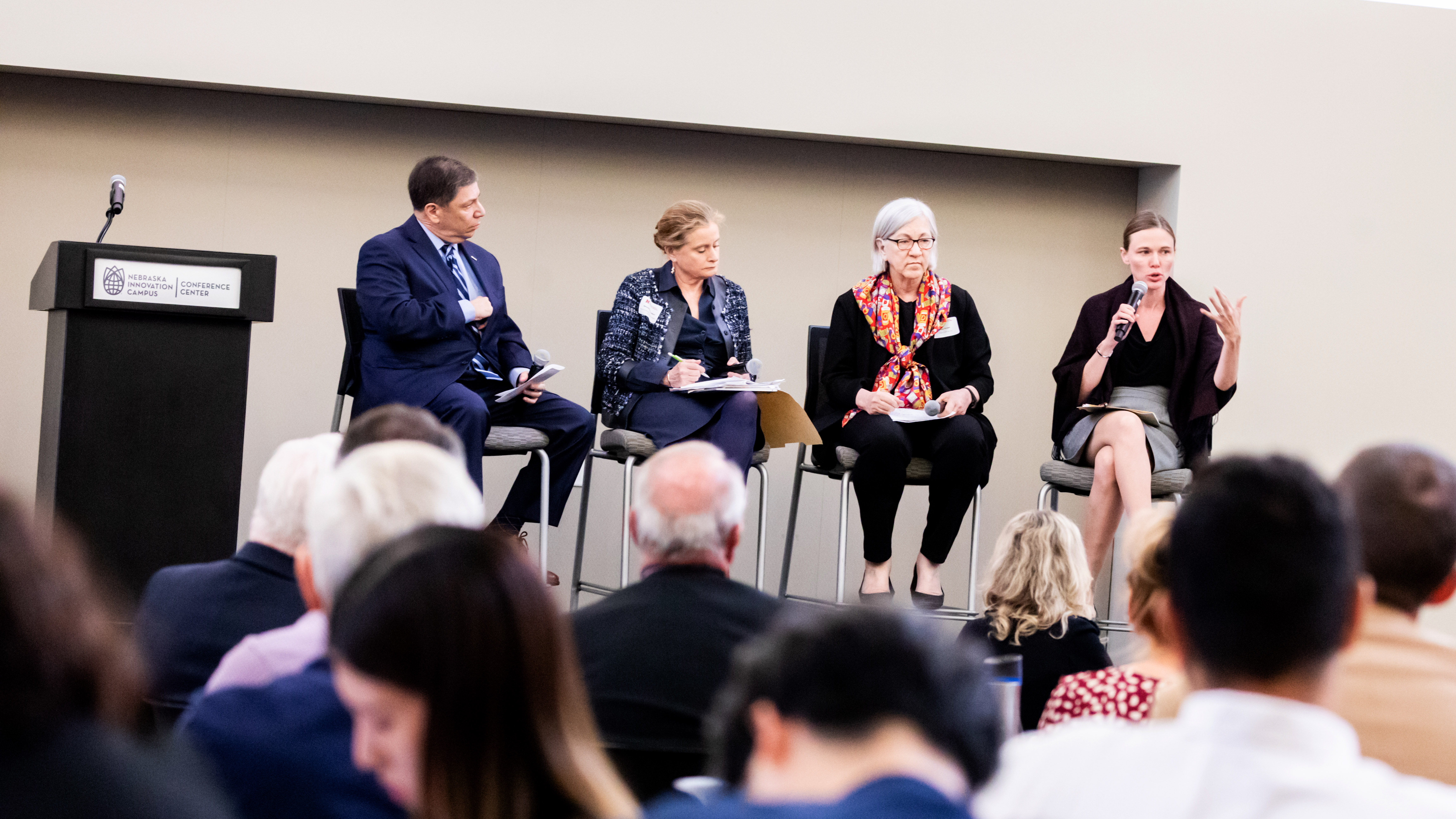 Four panelists — a man and three women — speak to a crowd.