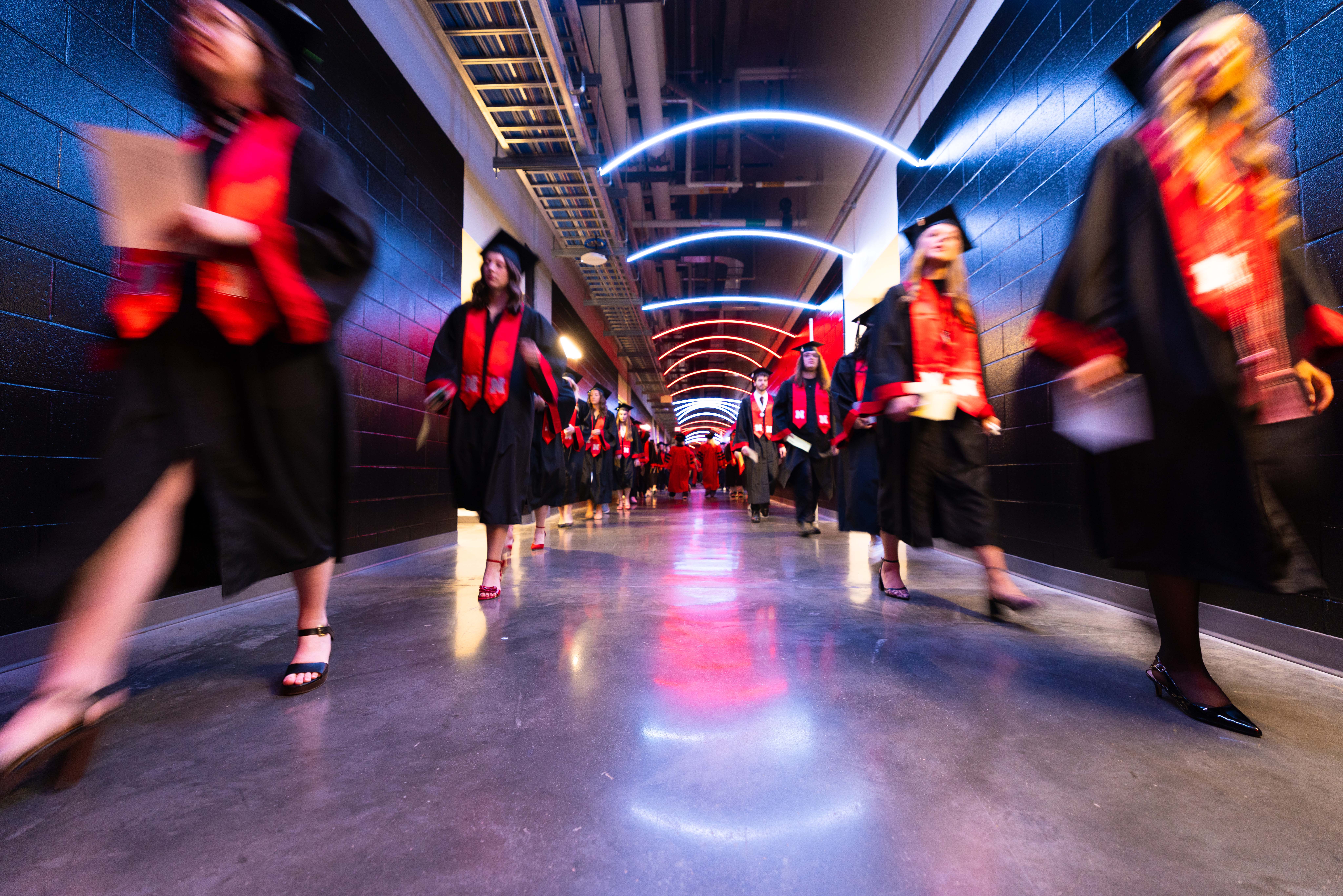 Two lines of graduates walk through a hallway in Pinnacle Bank Arena.