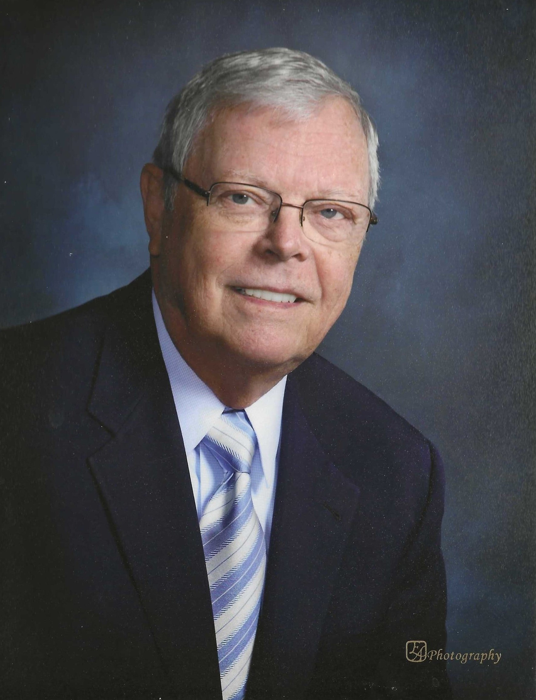 Color portrait of Scott W. Killinger, architect, educator and civic leader. He is wearing a dark blue sport coat over a white dress shirt and blue-and-white striped tie, with glasses.