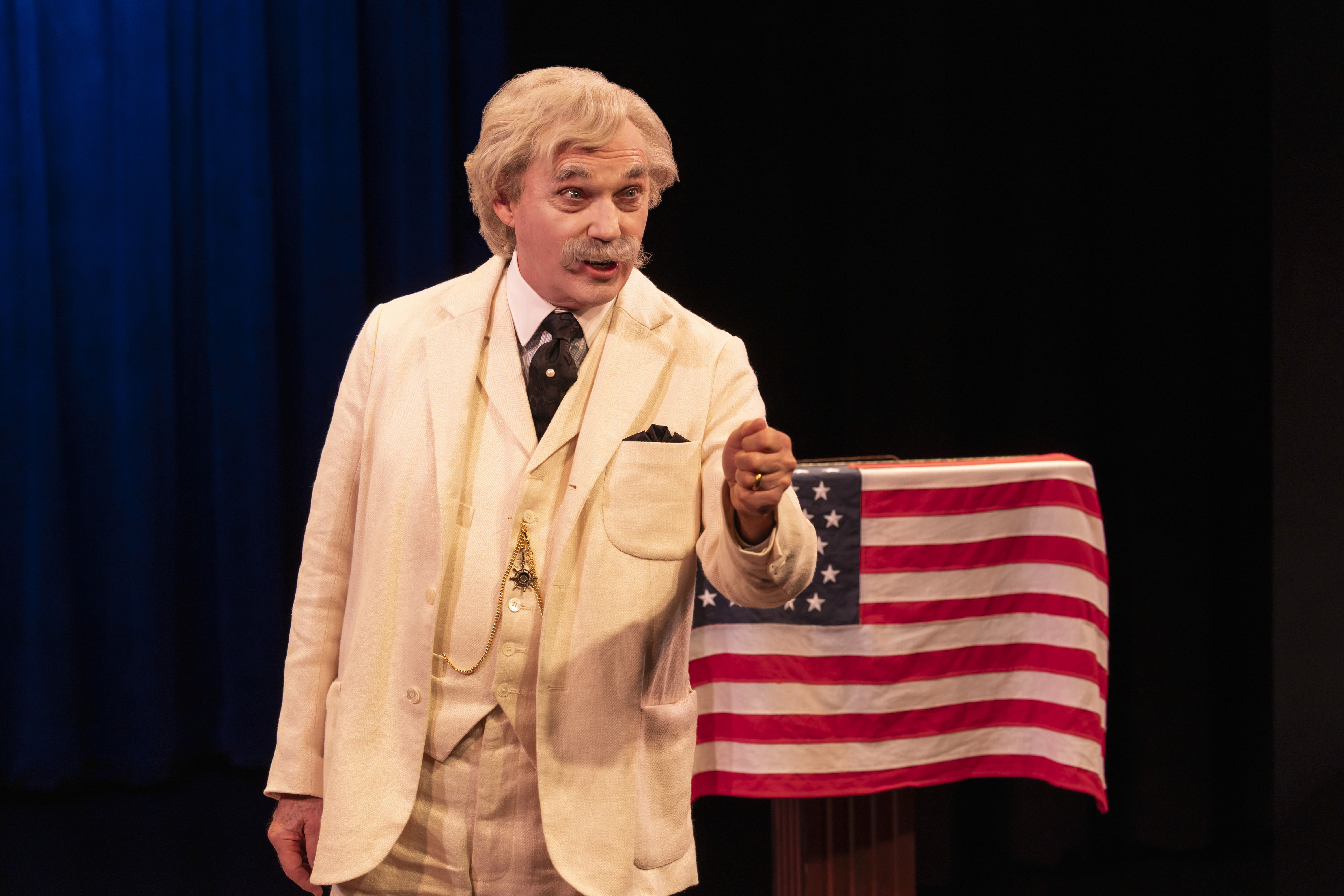 Actor Richard Thomas appears as Mark Twain, wearing a white suit, with an old American flag in the background.