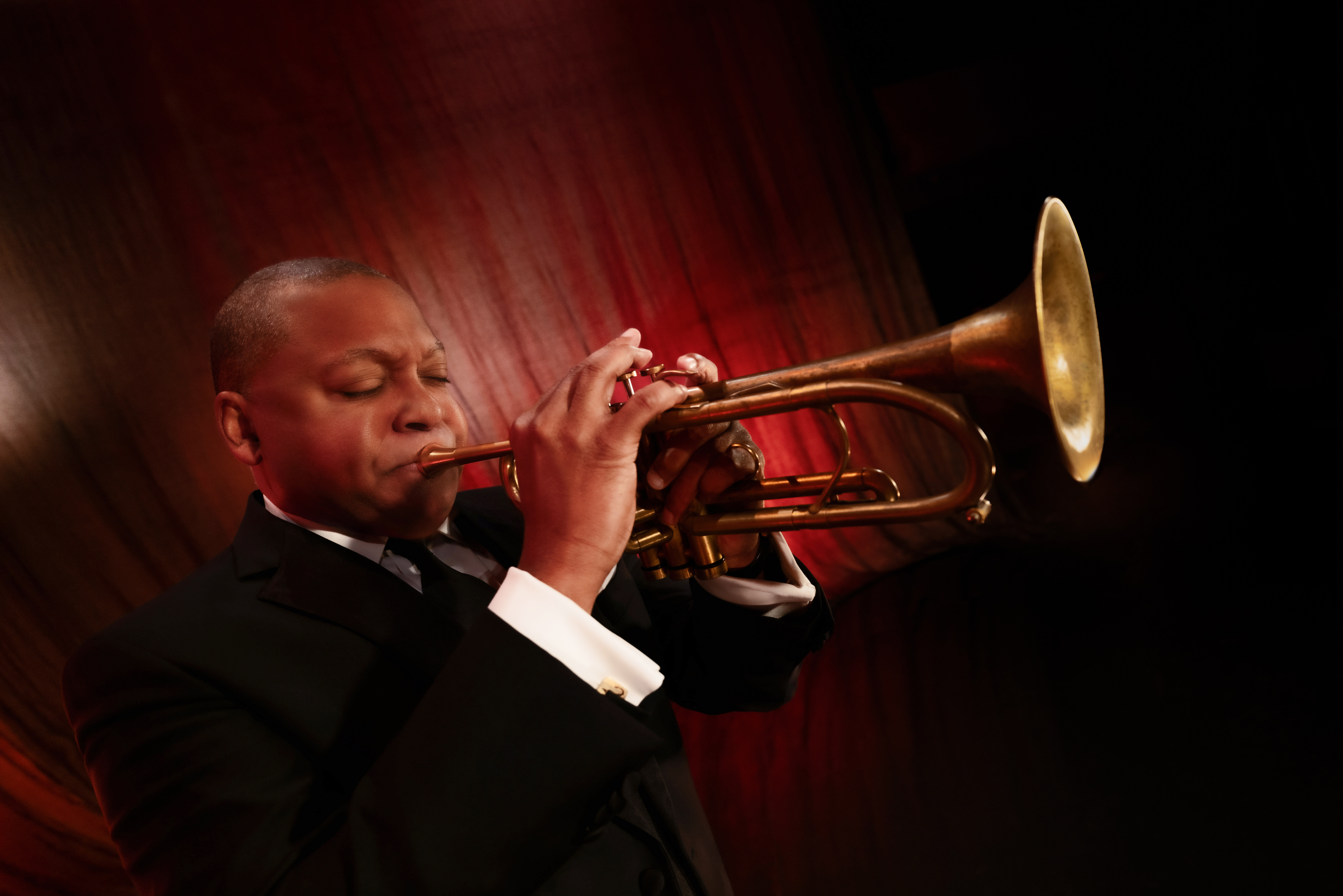 Wynton Marsalis, wearing a black-and-white suit, plays a trumpet.