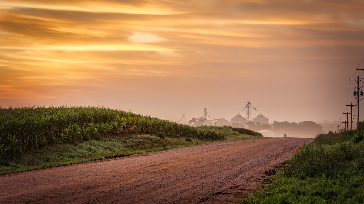 A farm can be seen along a country road under a cloudy sky.