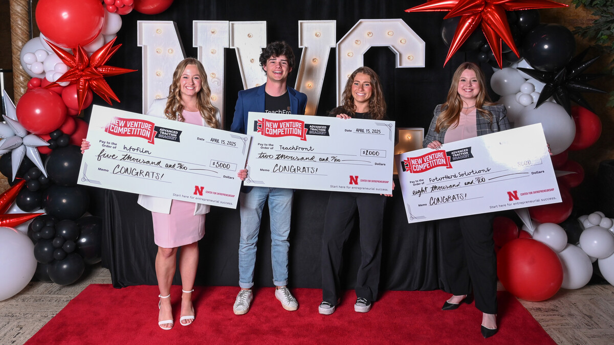Three young women and a young man hold oversized checks in front of the letters "NVC" and red and white balloons.
