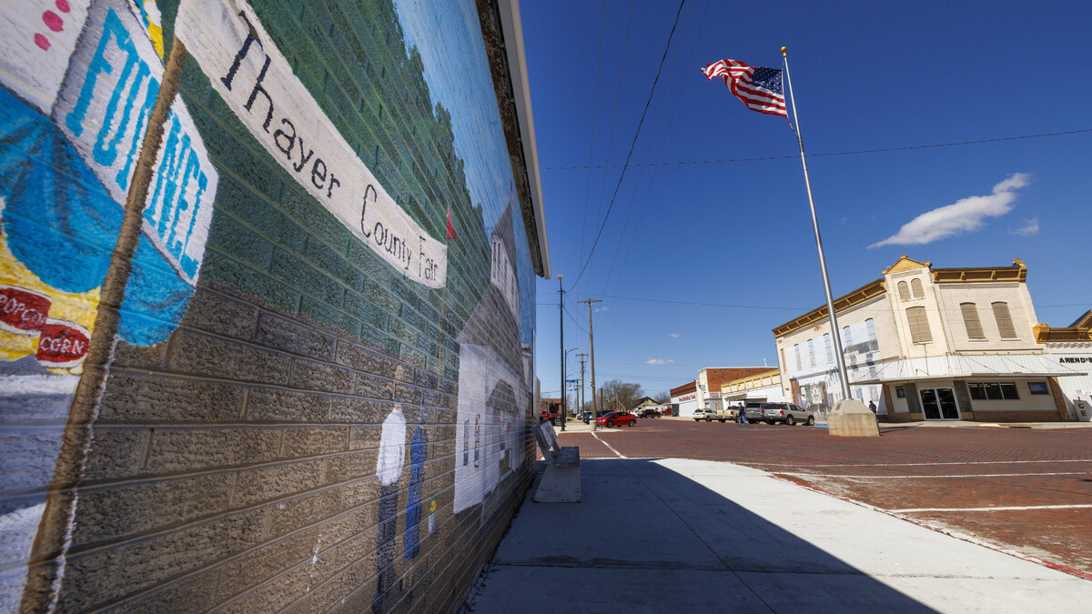 A Thayer County mural is painted on a brick wall in downtown Deshler, Nebraska. An American flag flies in the background.