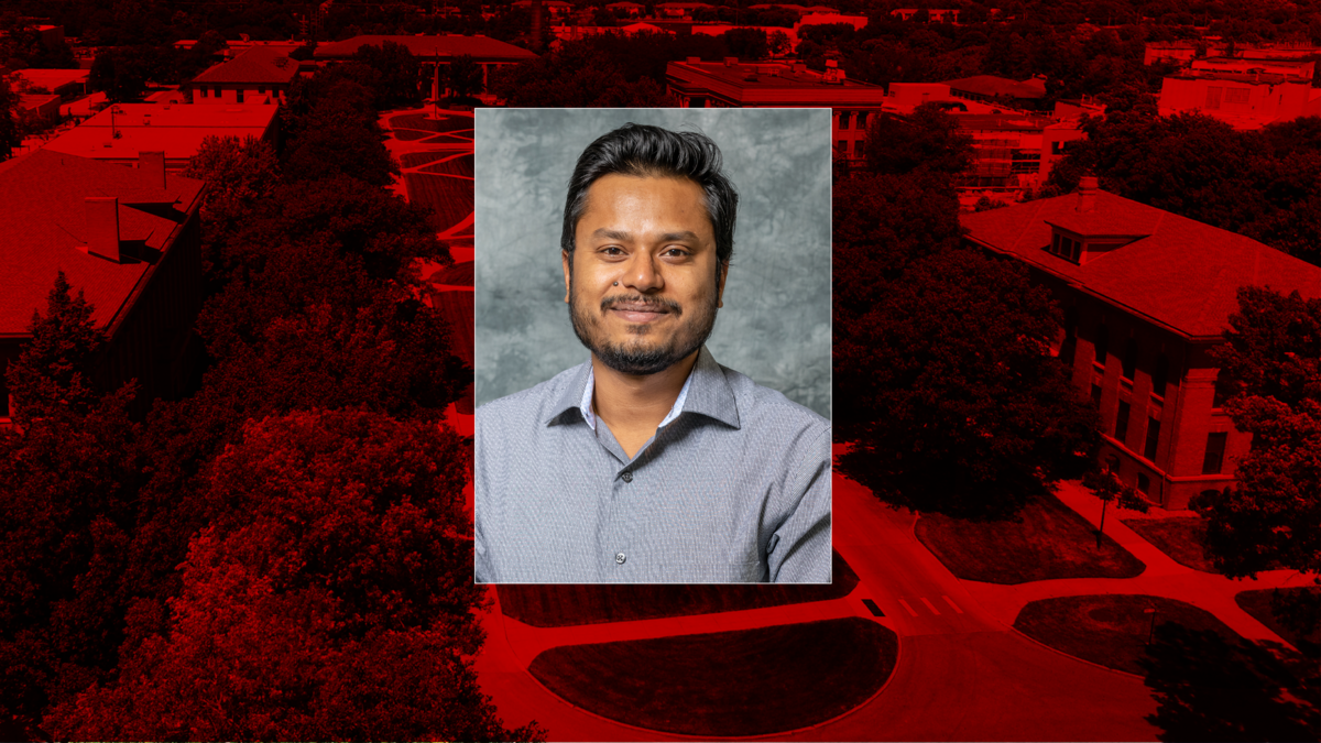 Portrait of Ankit Chandra, wearing a light gray button-up shirt, smiling in front of a neutral gray background. The image is centered over a red-tinted aerial view of the University of Nebraska–Lincoln’s East Campus.