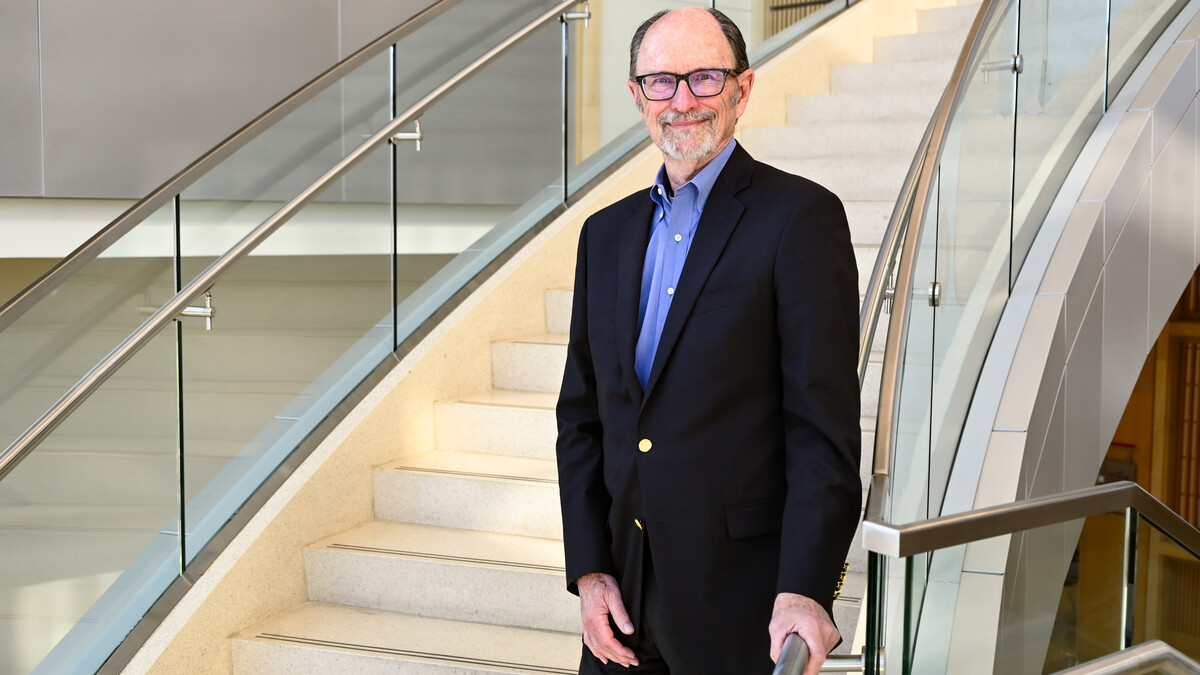 A man stands on a staircase next to a chrome railing and glass encasement.