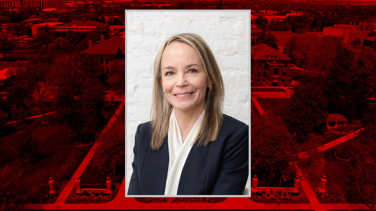 Professional headshot of Julie Callahan, a woman with blonde hair wearing a dark blazer and light blouse, centered over a red-tinted aerial image of the University of Nebraska–Lincoln campus.