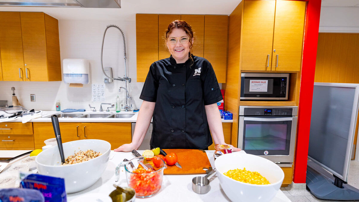 Ellyn McCarter stands and smiles in a test kitchen on campus during a food demonstration for students and staff.