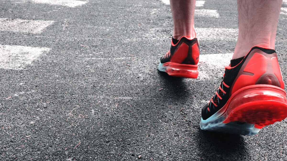 A man running in red tennis shoes on blacktop.