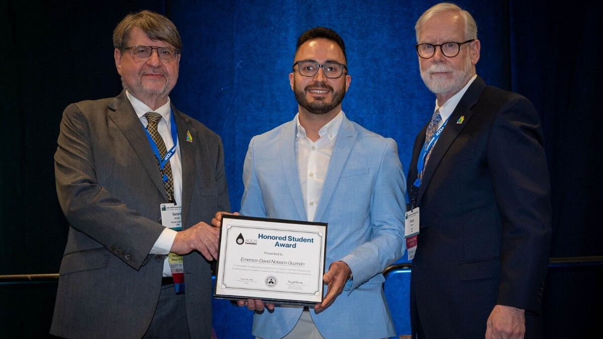 Emerson David Nolasco Guzmán, standing between AOCS President Gerard Baillely and CEO Patrick Donnelly, receives the 2025 AOCS Honored Student Award at the Annual Meeting in Portland, Oregon. All three are wearing business attire and smiling at the camera.