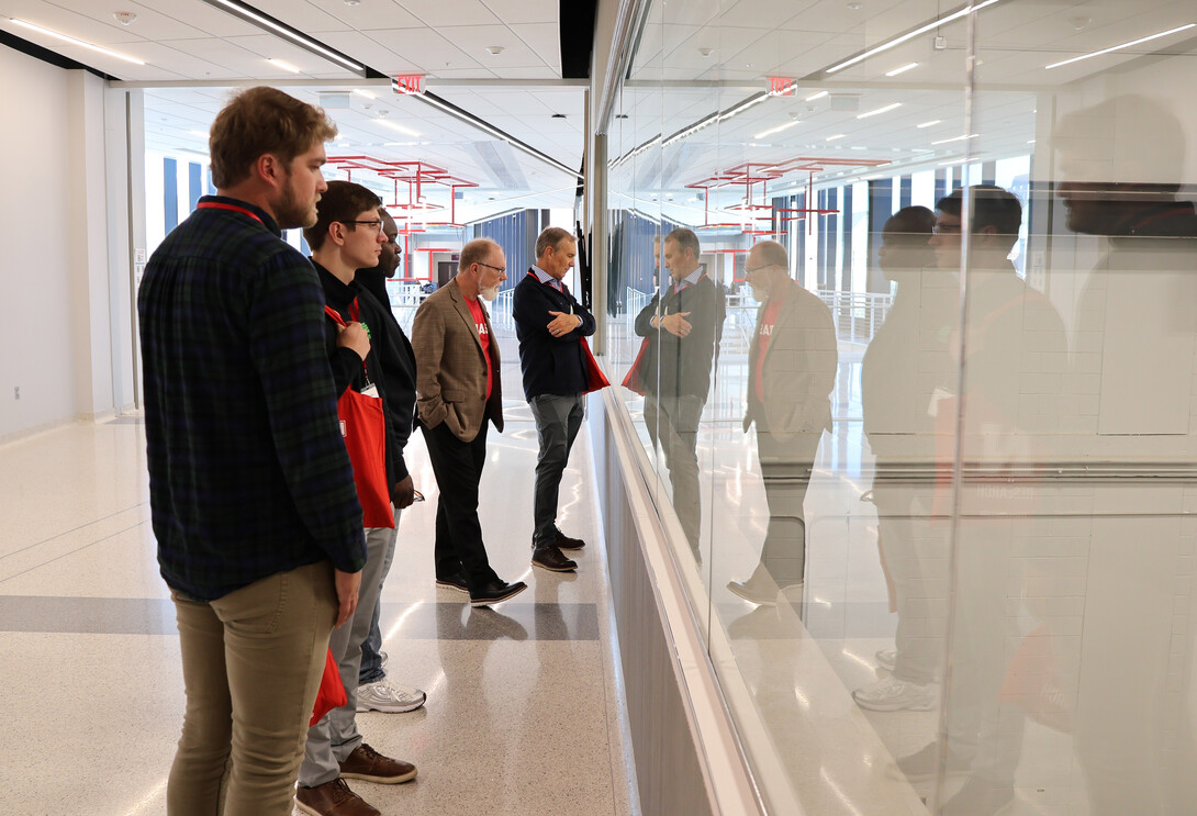 Five men stand in a hallway, looking into a room.