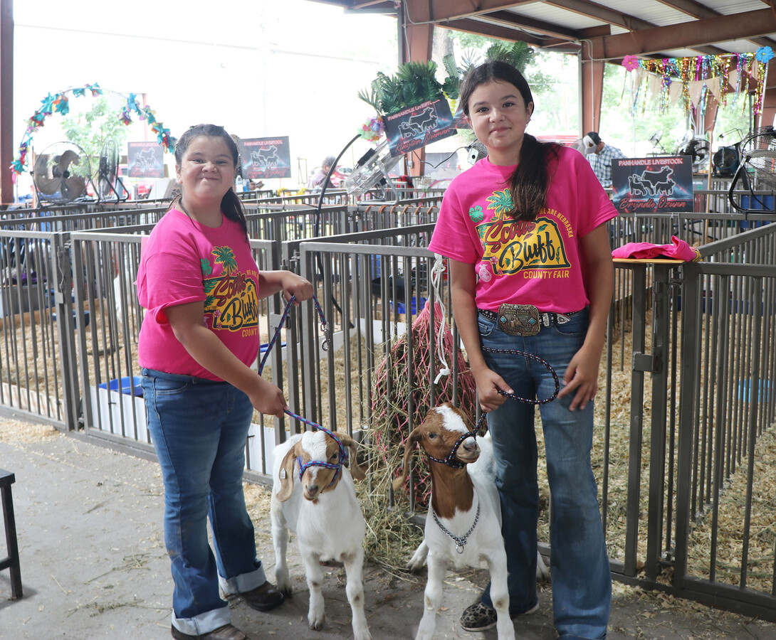 two girls standing next to their goats