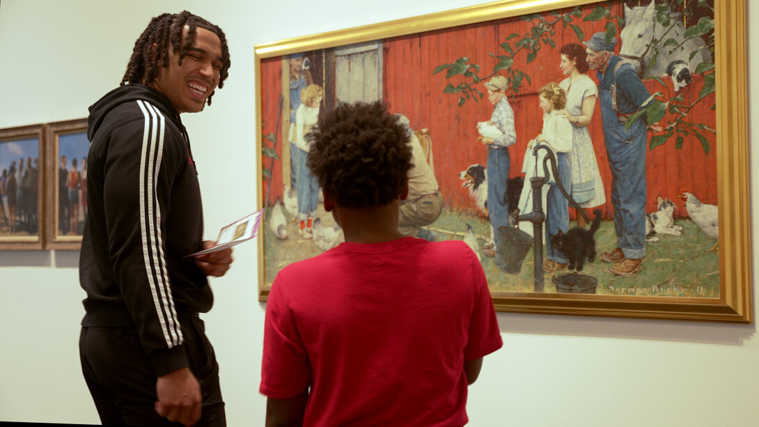 A young man and a child stand in front of a painting.