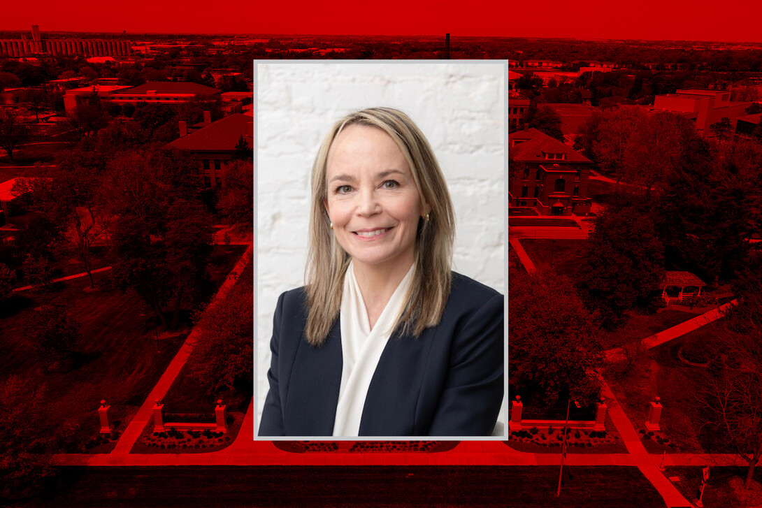 Professional headshot of Julie Callahan, a woman with blonde hair wearing a dark blazer and light blouse, centered over a red-tinted aerial image of the University of Nebraska–Lincoln campus.