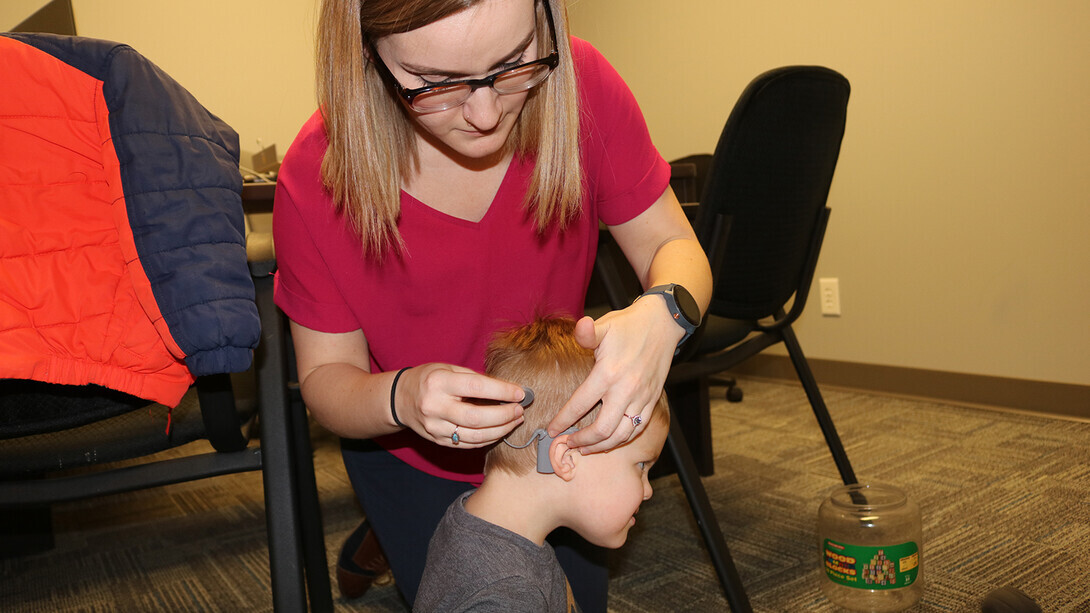 A student in the Department of Special Education and Communication Disorders adjusts the hearing aid of a young boy.