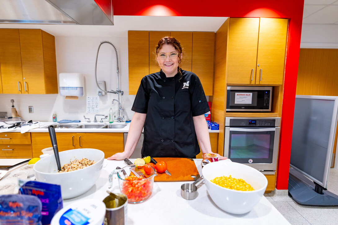 Ellyn McCarter stands and smiles in a test kitchen on campus during a food demonstration for students and staff.