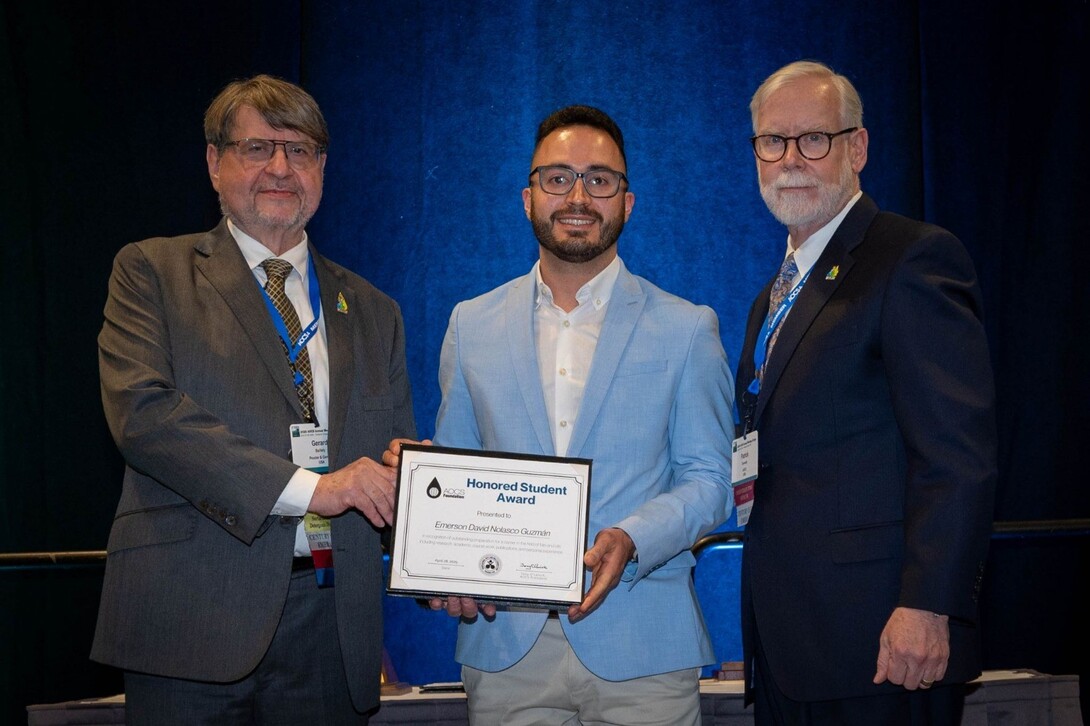 Emerson David Nolasco Guzmán, standing between AOCS President Gerard Baillely and CEO Patrick Donnelly, receives the 2025 AOCS Honored Student Award at the Annual Meeting in Portland, Oregon. All three are wearing business attire and smiling at the camera.